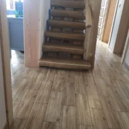 Drewniane schody z balustradą z pnia drzewa na podłodze wyłożonej płytkami imitującymi drewno, widok z dołu.