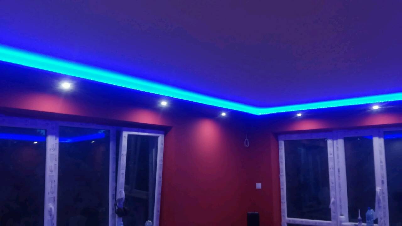 Nowoczesne oświetlenie sufitowe LED w kolorze niebieskim, zamontowane w pomieszczeniu z czerwonymi ścianami i białymi oknami.