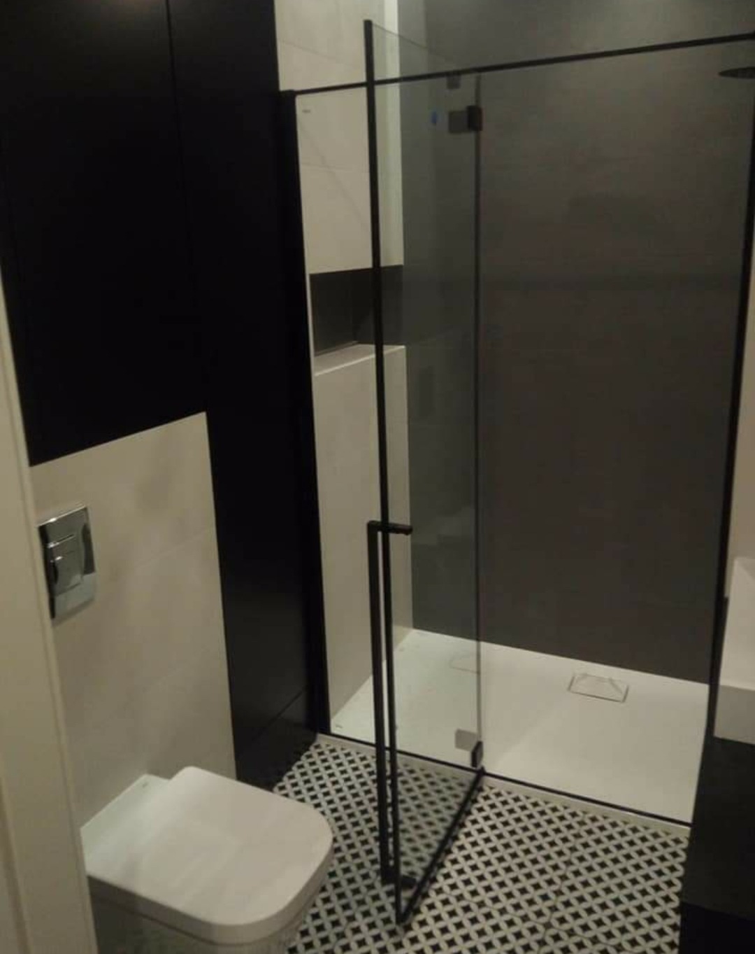 Nowoczesna łazienka z kabiną prysznicową ze szklanymi drzwiami z czarnymi ramami, białą ceramiką i czarno-białą mozaiką na podłodze.