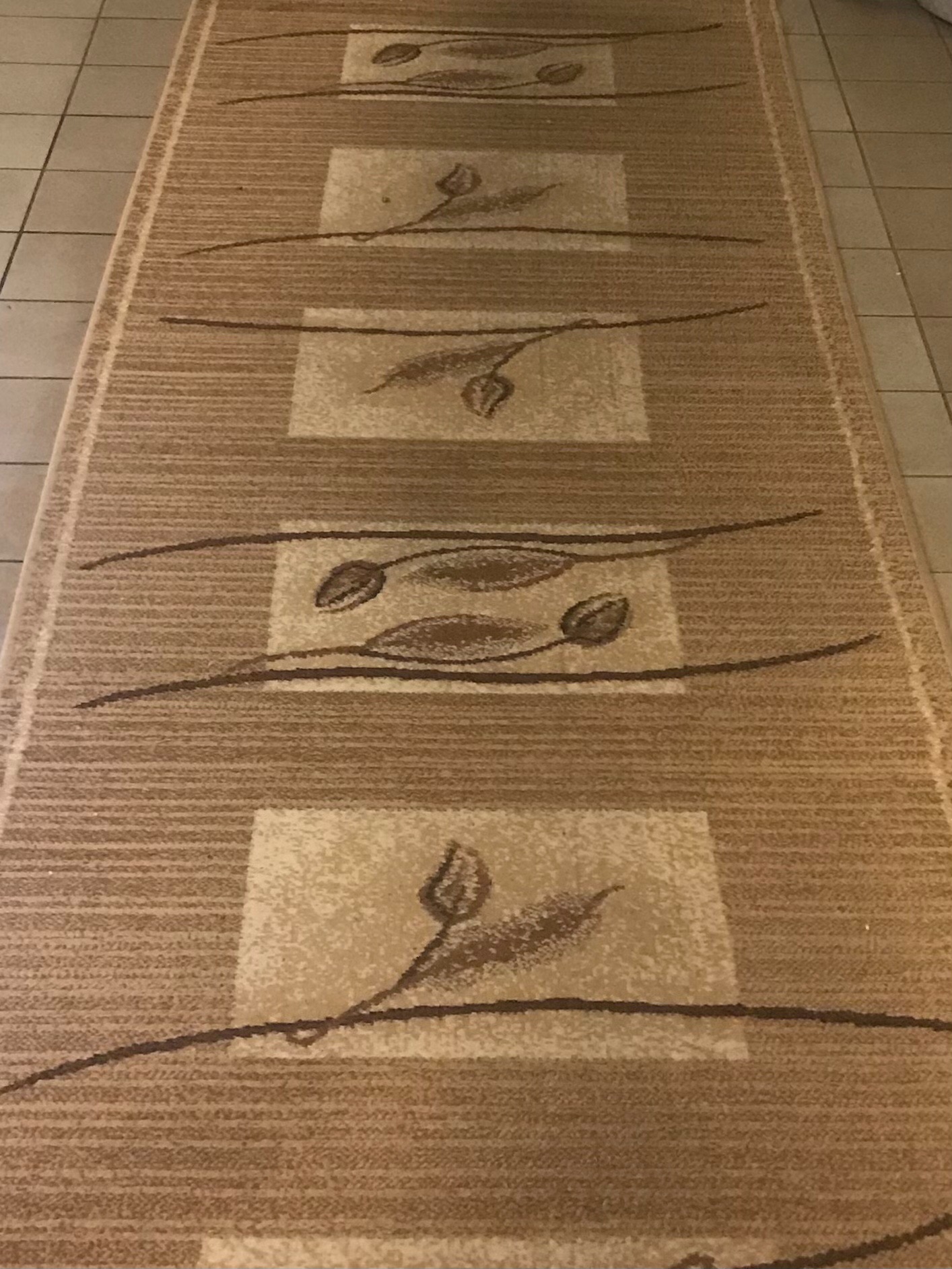 Beżowy dywanik z geometrycznym wzorem kwiatowym leżący na kafelkach podłogowych.