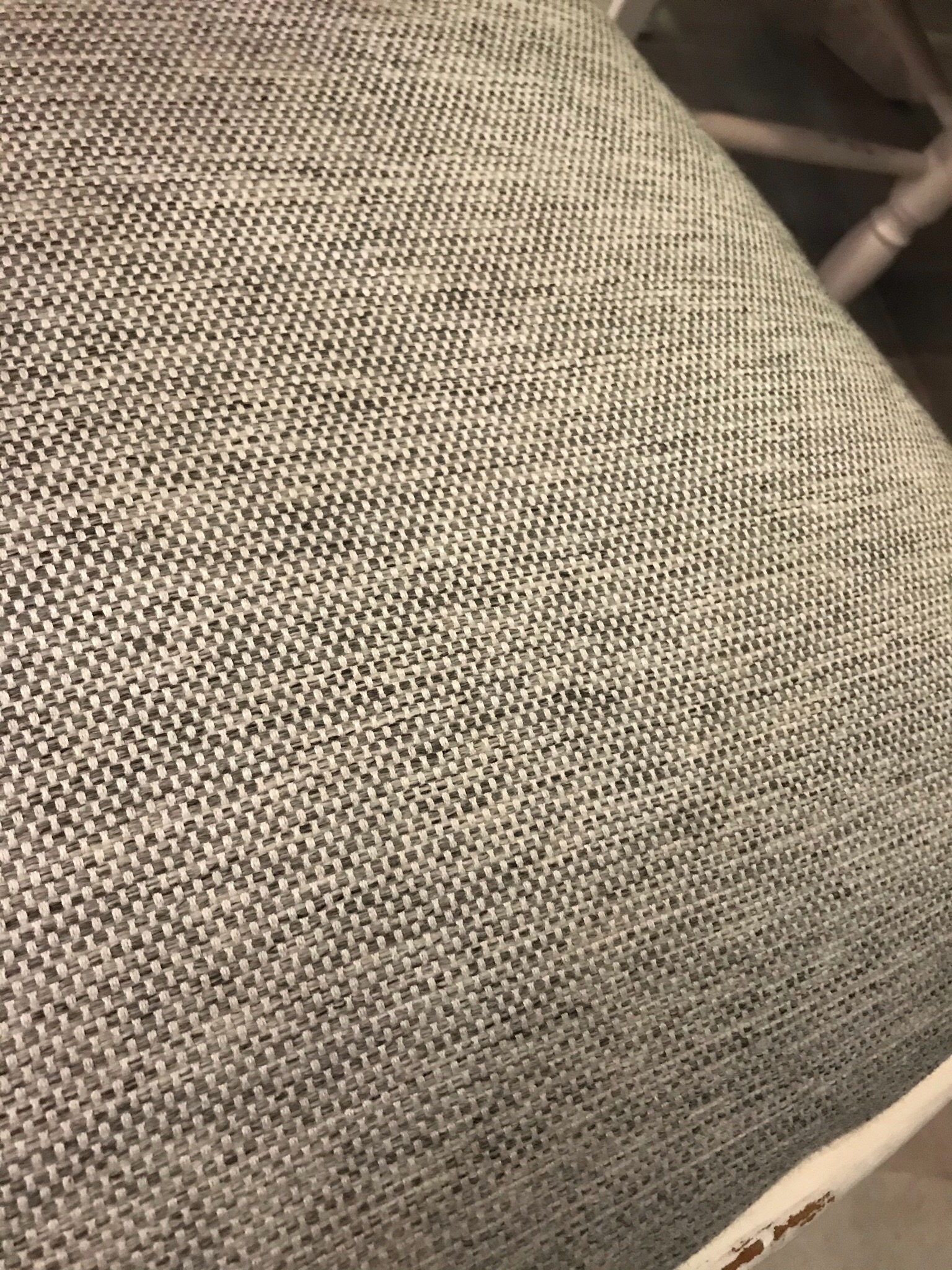 Zbliżenie na szarą, plecioną tapicerkę siedziska krzesła z widoczną strukturą materiału.