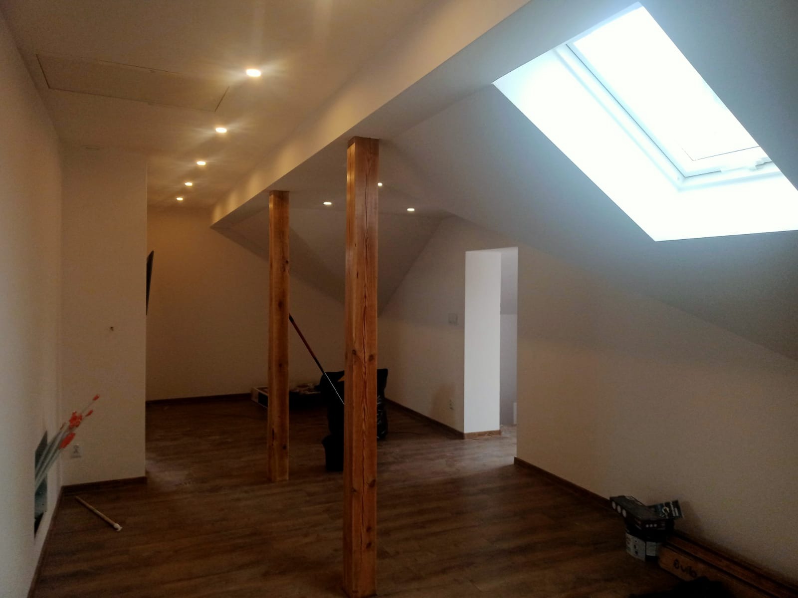 Poddasze po remoncie z drewnianą podłogą, dwoma drewnianymi słupami, oknem dachowym i rzędem punktowych lamp sufitowych
