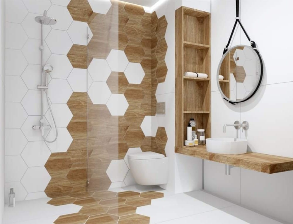 Nowoczesna łazienka z heksagonalnymi płytkami w odcieniach bieli i drewna, kabina prysznicowa ze szklaną ścianką, okrągłe lustro zawieszone na pasku i drewniana półka z umywalką.