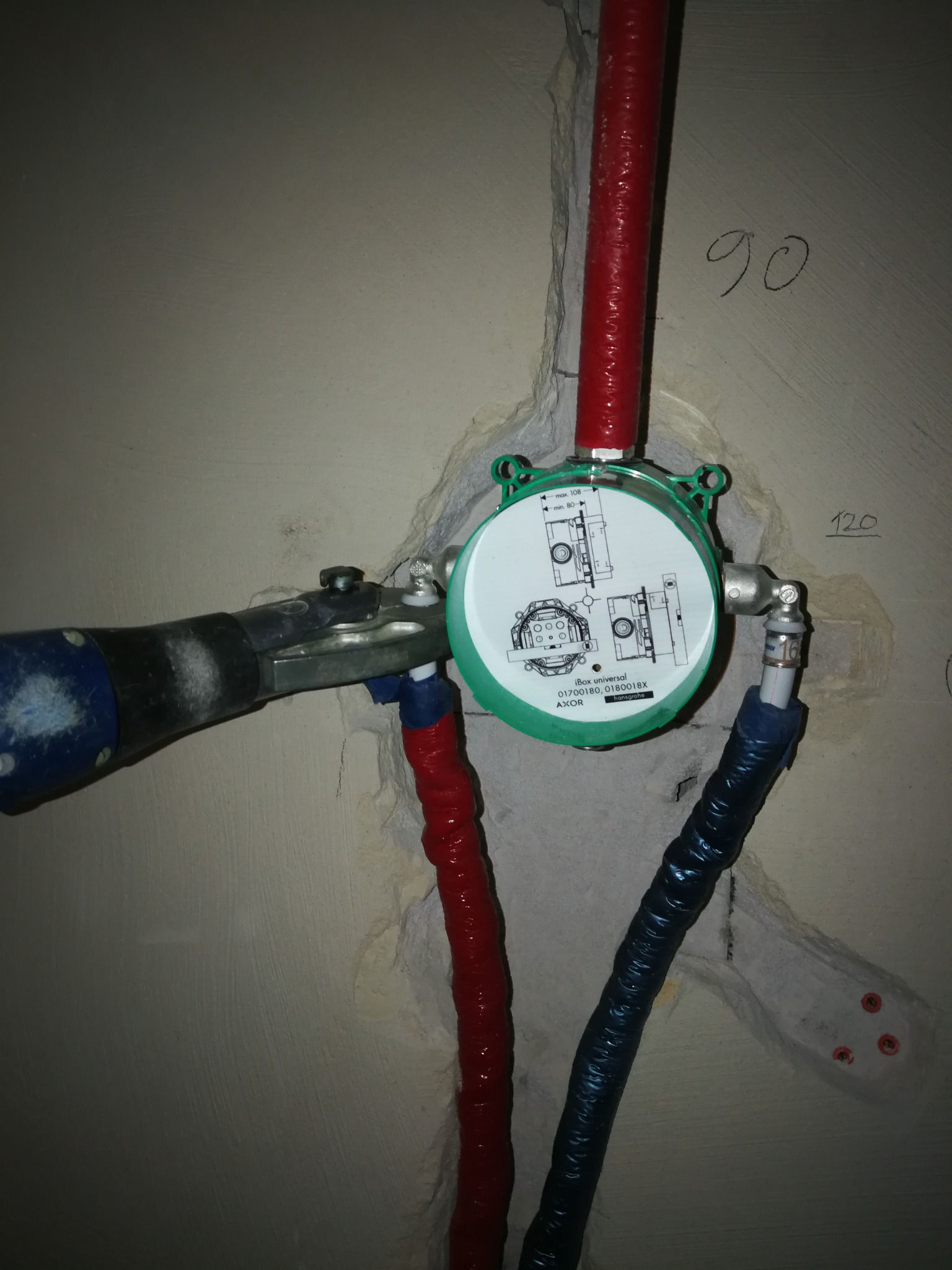 Montaż podtynkowego zaworu termostatycznego Hansgrohe iBox Universal z podłączonymi rurami ciepłej i zimnej wody w surowej ścianie łazienki, widoczne oznaczenia wysokości.