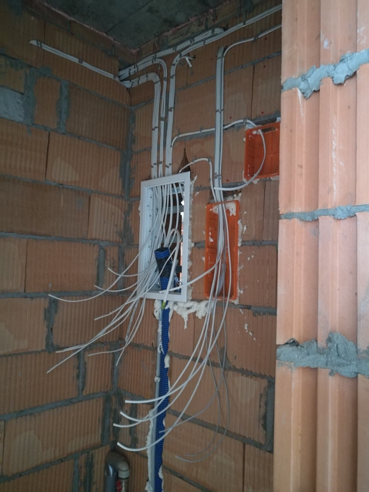 Rozprowadzenie przewodów elektrycznych w ścianie z pustaków ceramicznych, widoczne puszki instalacyjne i peszel z kablami.