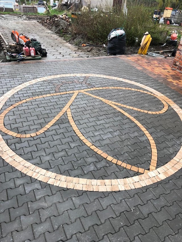 Ułożona kostka brukowa z dekoracyjnym motywem w kształcie okręgów z jaśniejszej kostki, widoczne narzędzia pracy w tle.