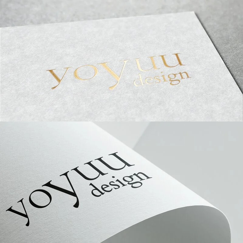Dwa warianty logo 'yoyUU design' na białym papierze z widoczną fakturą: złote tłoczenie na górze i czarny nadruk na dole, z delikatnym podwinięciem rogu papieru.