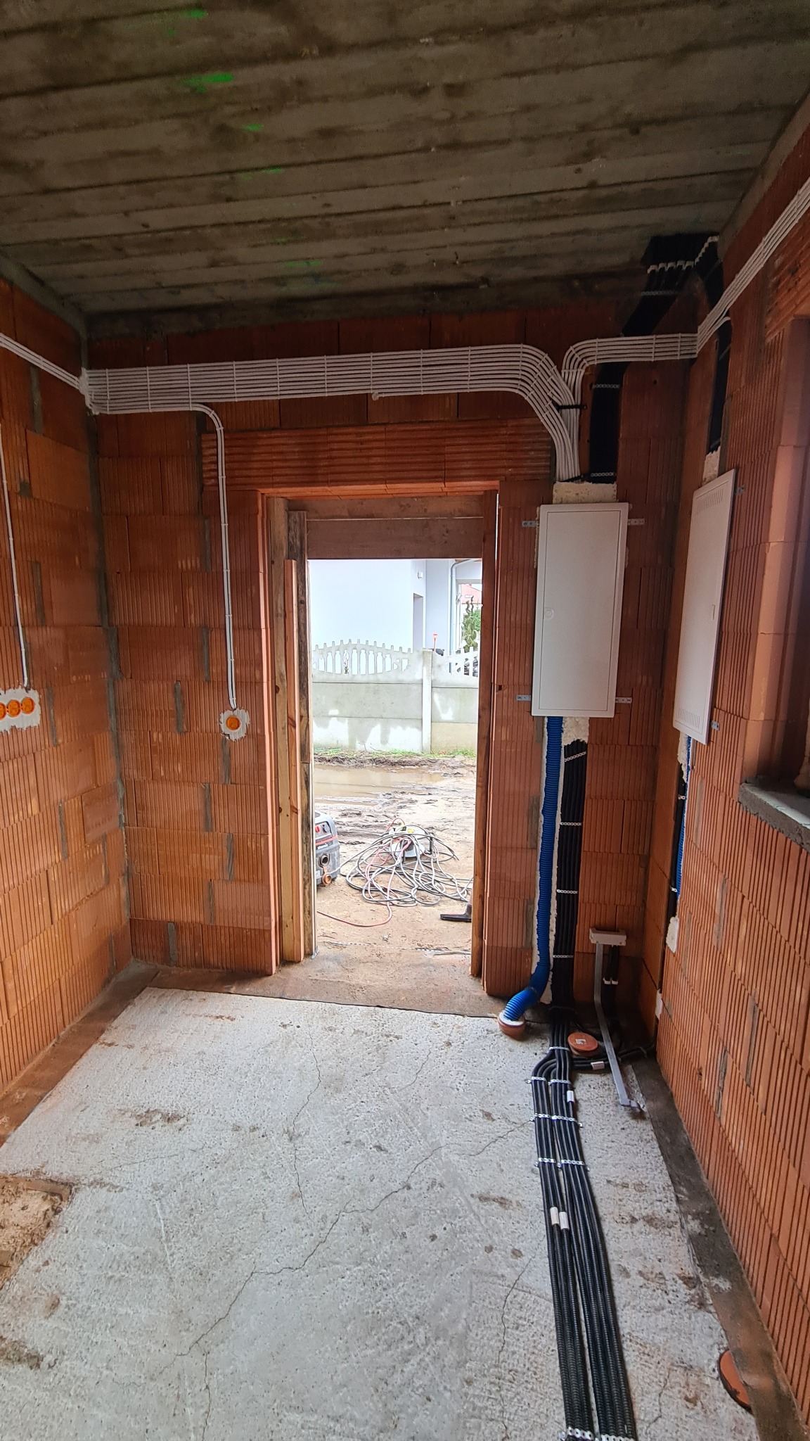 Wnętrze w trakcie prac elektrycznych: widoczne kable prowadzone po ścianach z cegły, puszki instalacyjne, skrzynka rozdzielcza oraz narzędzia na zewnątrz budynku.