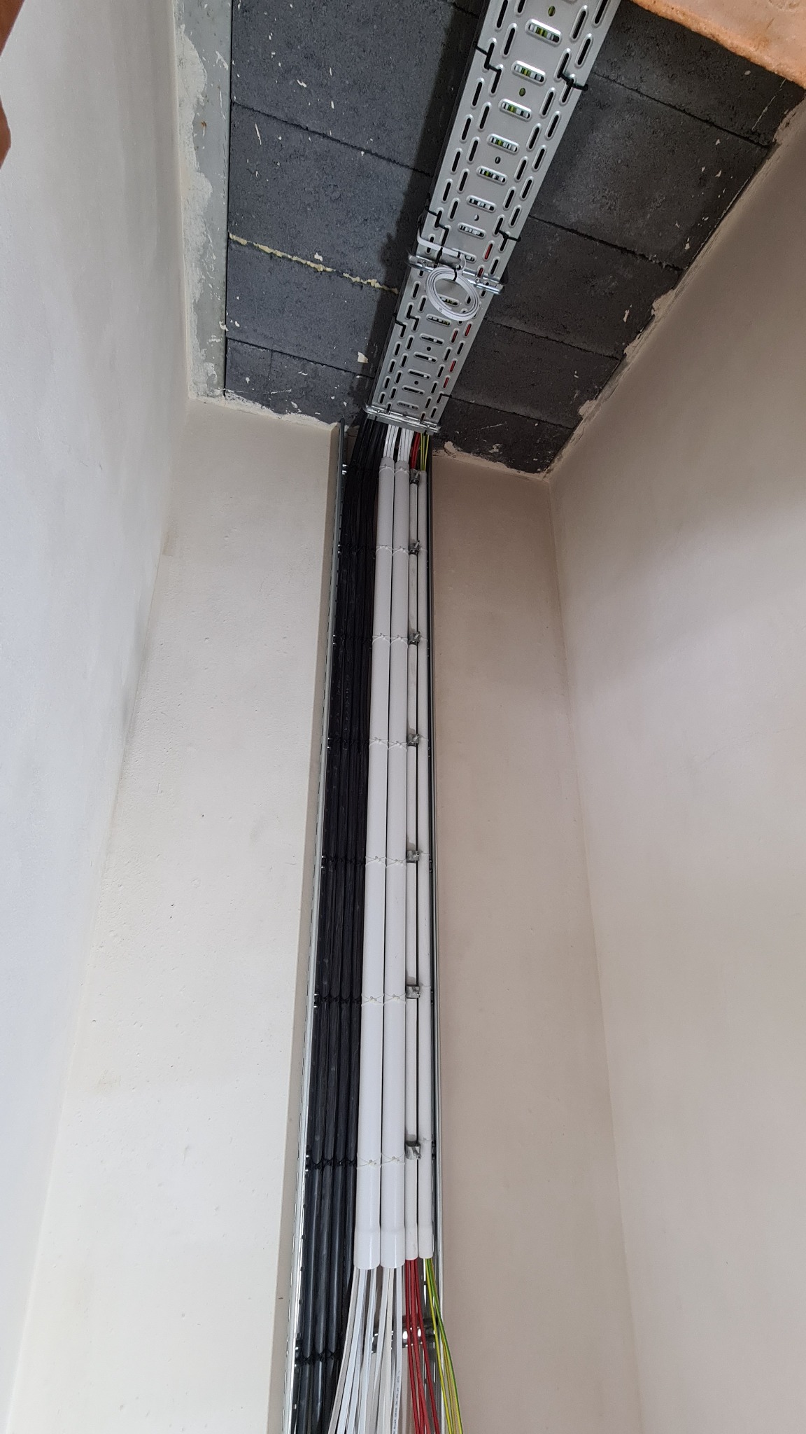 Metalowa korytka kablowa zamontowana pod sufitem, prowadząca wiązki kabli w peszlach i bez, w nowym budynku w trakcie wykańczania.