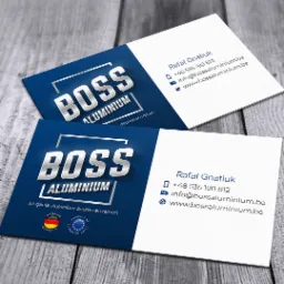 Dwie wizytówki firmy BOSS Aluminium na drewnianym tle, z logo w kolorze niebieskim i srebrnym, zawierające dane kontaktowe oraz informację o eleganckich aluminiowych drzwiach i oknach.