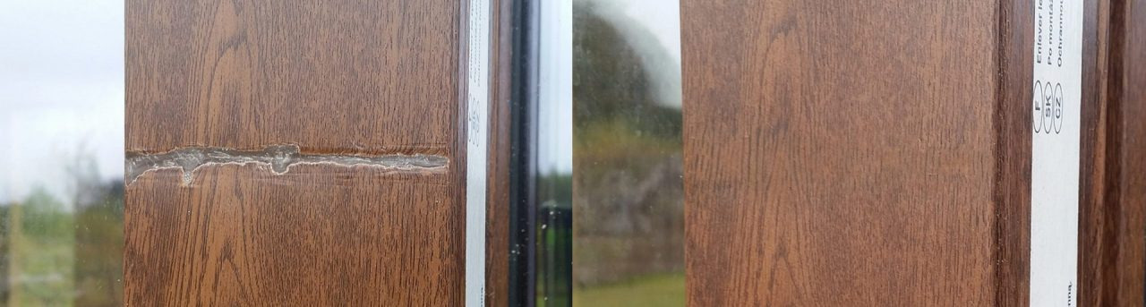 Uszkodzona, brązowa rama okienna z widocznym pęknięciem i ubytkiem, z zewnątrz widok na zieleń. Na ramie naklejka z informacjami o produkcie.