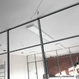 Montaż oświetlenia biurowego: widok na sufit z zamontowanymi panelami LED w przestrzeni biurowej z aluminiowymi profilami konstrukcyjnymi, widoczna drabina i przygotowana instalacja elektryczna.