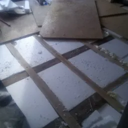 Ocieplenie poddasza: białe płyty styropianowe umieszczone między drewnianymi belkami, widoczne ślady pianki montażowej i fragmenty płyt OSB na podłodze.