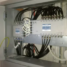 Rozdzielnica sygnału telewizyjnego z licznymi kablami koncentrycznymi, zamontowana w metalowej szafce, z widocznym uziemieniem.