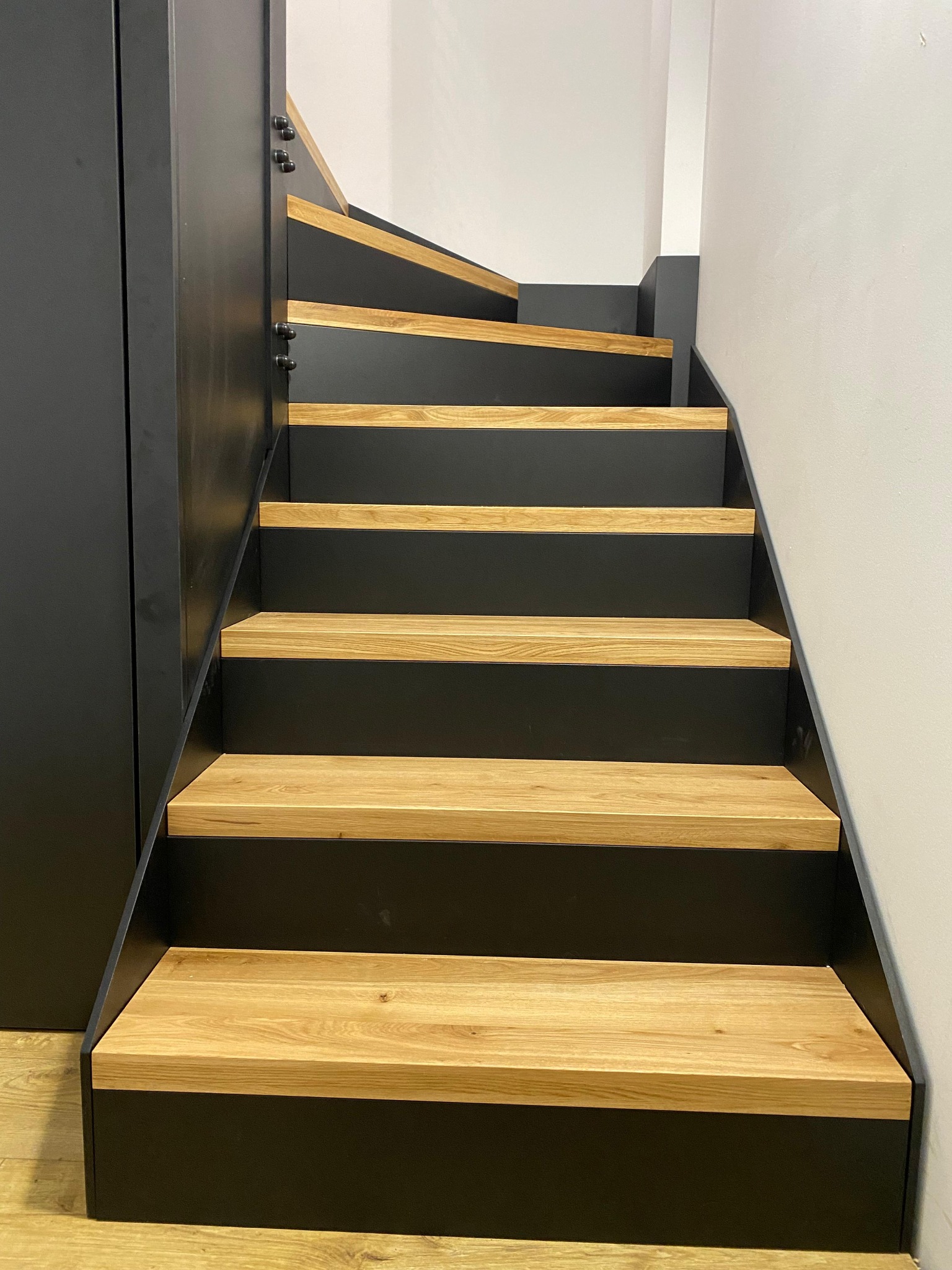 Nowoczesne schody z drewnianymi stopniami i czarną metalową konstrukcją, widok z dołu, oświetlenie naturalne, minimalistyczny design.