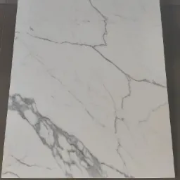 Biały brodzik z imitacją marmuru, z liniowym odpływem, ułożony na szarych płytkach podłogowych.