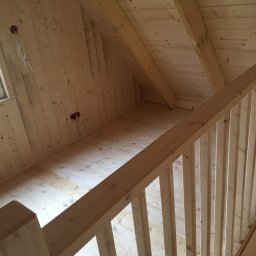 M+T DOMY Tomasz Minge - Surowe wnętrze poddasza z drewnianą konstrukcją szkieletową i schodami, widoczne gniazdka elektryczne z wystającymi kablami, surowe wykończenie.