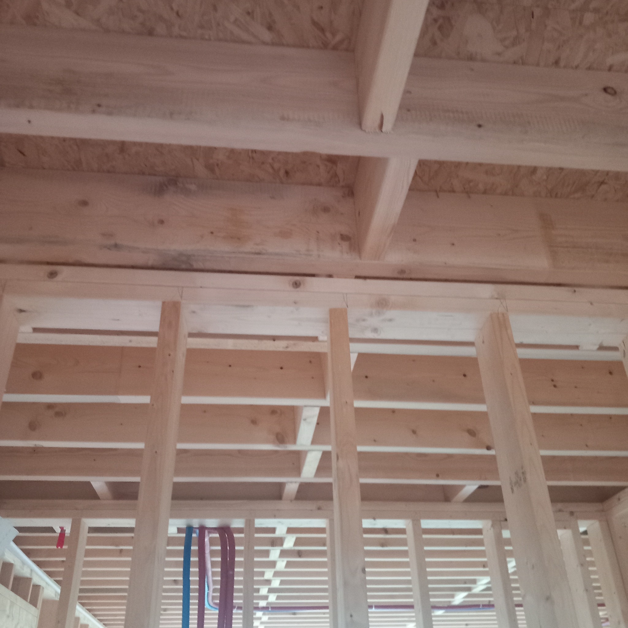 Konstrukcja drewniana szkieletu domu w trakcie budowy, widoczne belki stropowe i ściany z płyt OSB, instalacje w kolorowych peszlach.