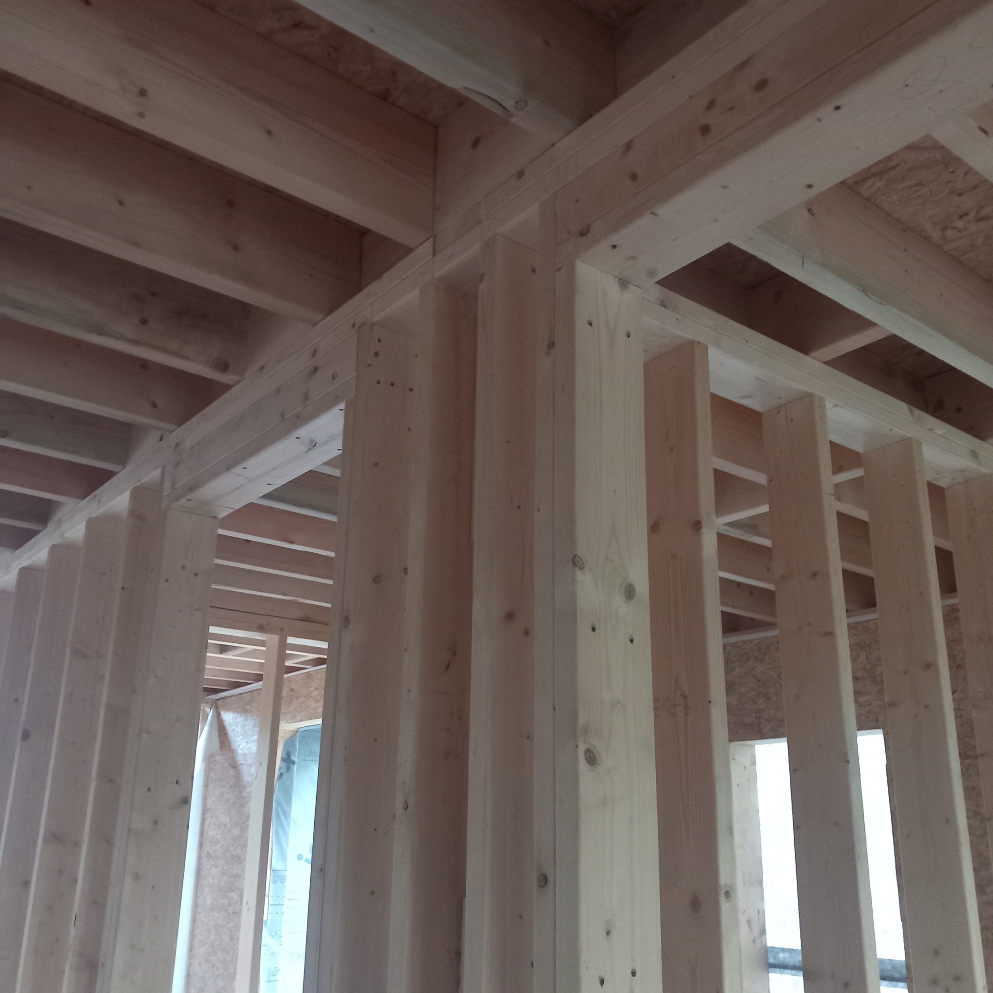 Surowe drewniane elementy konstrukcyjne w trakcie budowy domu, widoczne słupy i belki stropowe, jasne drewno, niedokończona konstrukcja.