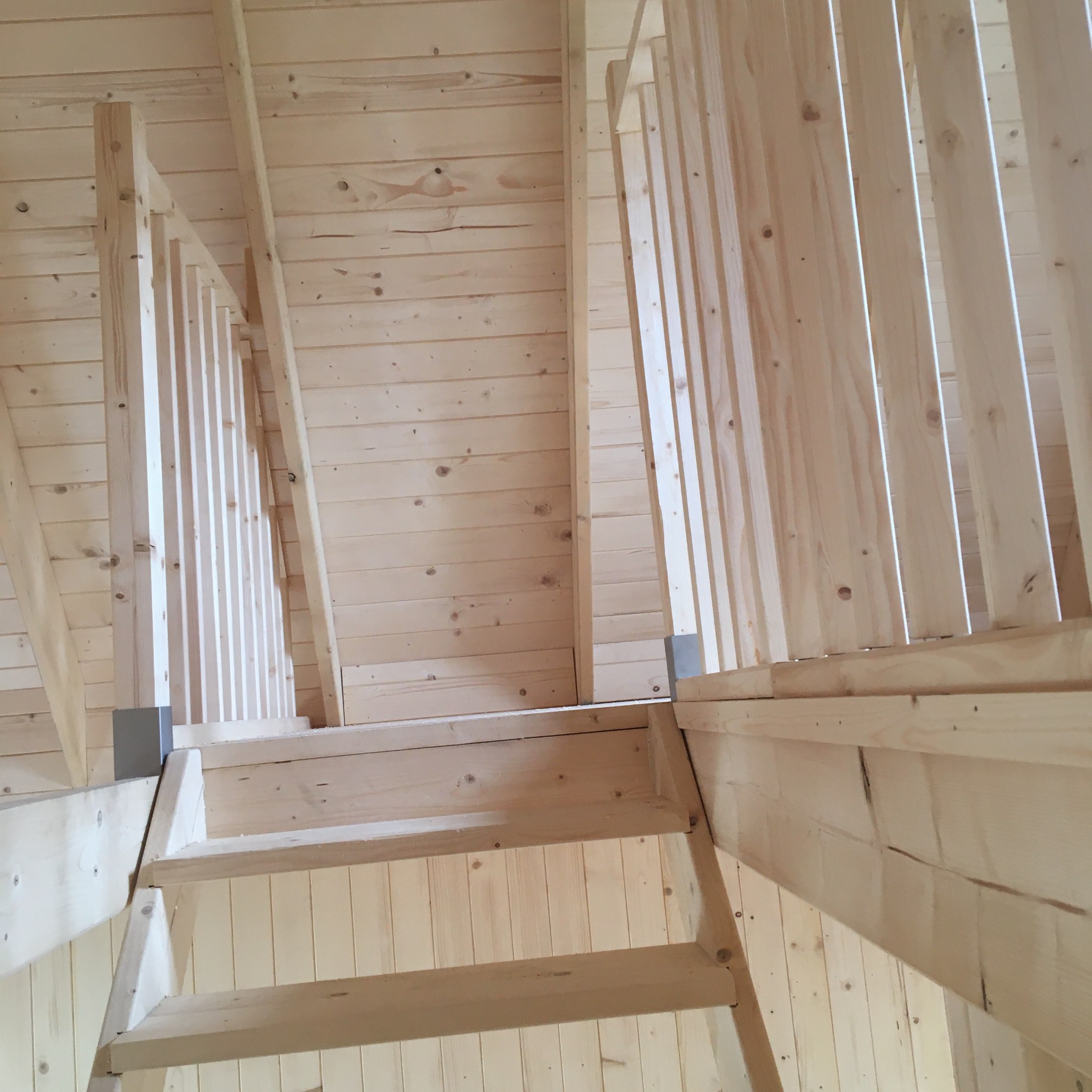 Wnętrze domu w konstrukcji szkieletowej z widocznymi drewnianymi schodami i balustradą, wykończone jasnym drewnem.