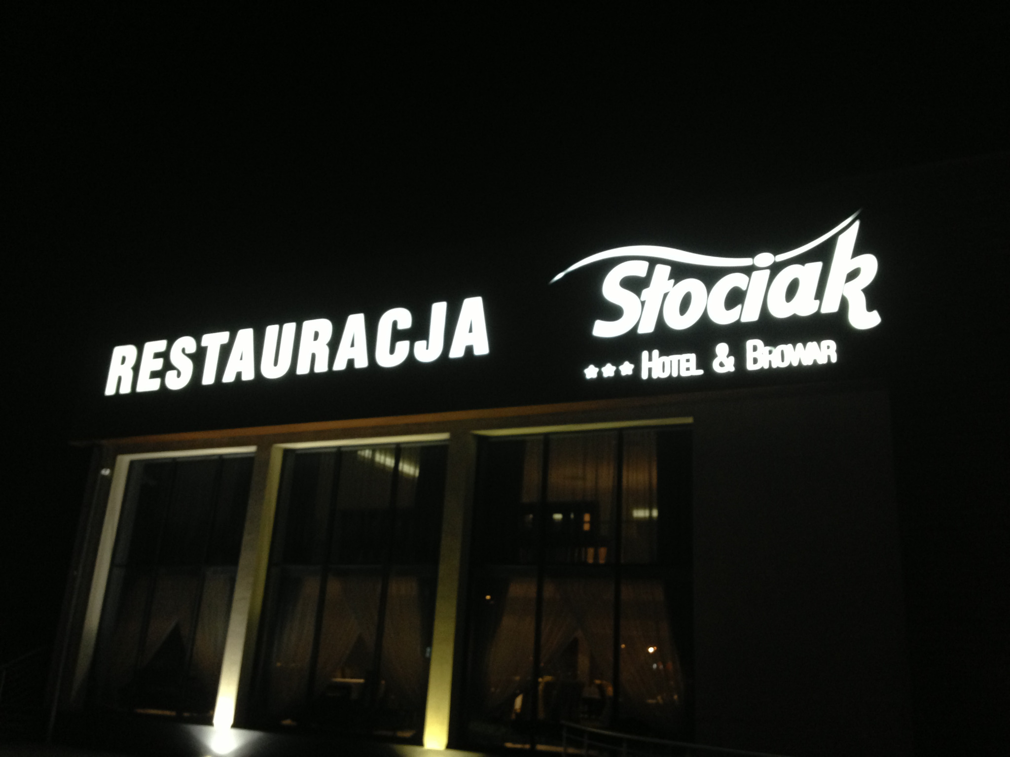 Świecący szyld restauracji i hotelu Stociak w nocy, widoczne okna budynku.