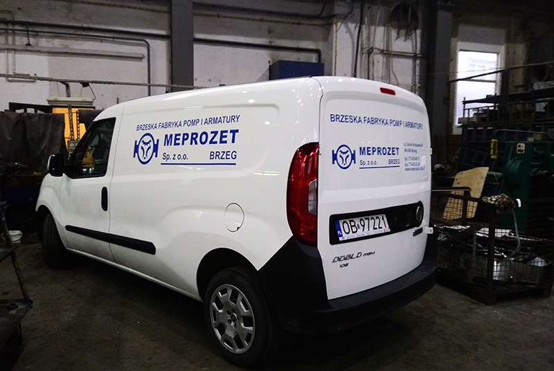Biały samochód dostawczy z niebieskim logo i nazwą firmy 'MEPROZET' z Brzegu, zaparkowany w hali produkcyjnej.