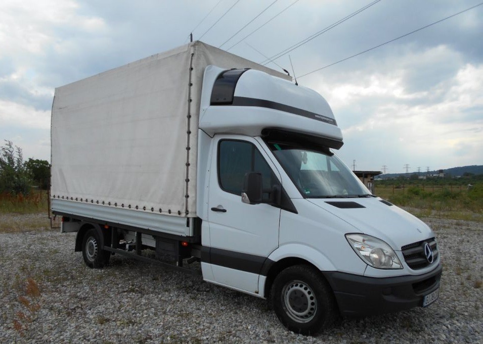 Biały samochód dostawczy Mercedes-Benz z plandeką na tle pochmurnego nieba i linii wysokiego napięcia.