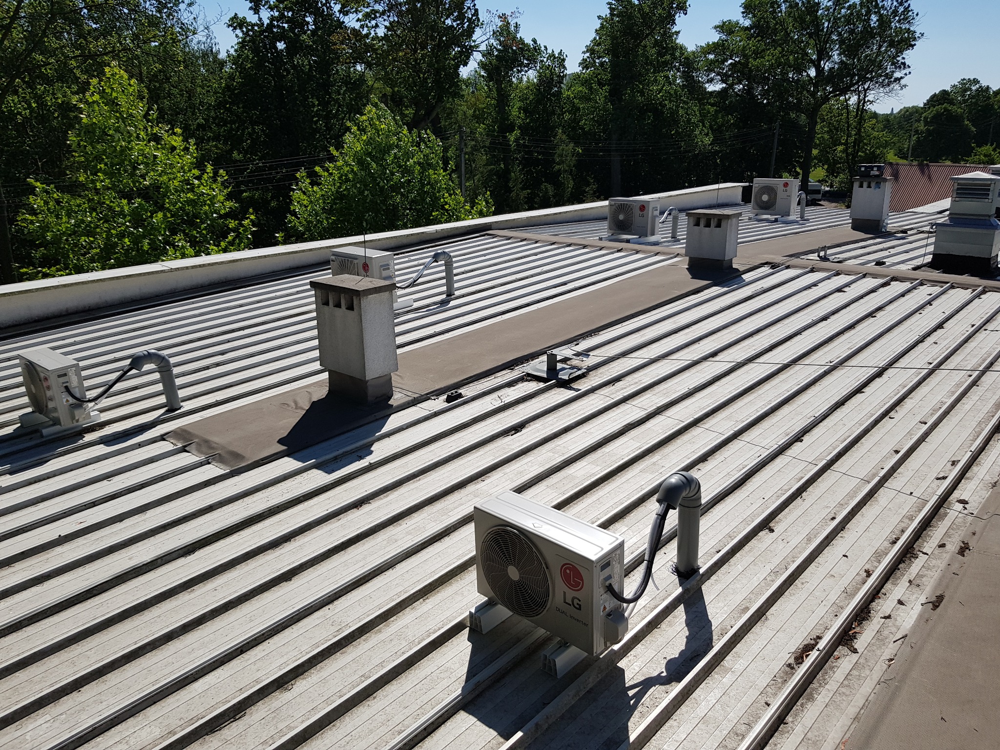 Rzut z góry na metalowy dach z kilkoma zewnętrznymi jednostkami klimatyzacji LG i pionowymi wylotami wentylacyjnymi