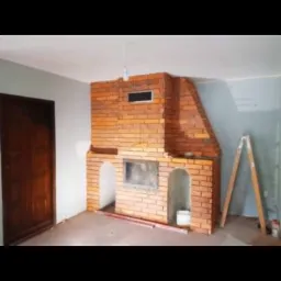 Wnętrze z murowanym kominkiem z cegły w trakcie budowy, widoczna drabina oparta o ścianę i niepomalowane ściany.