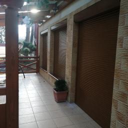 Łukasz Nowak - Zewnętrzne brązowe rolety zamontowane na elewacji budynku z cegieł, widok z zadaszonego tarasu z drewnianą konstrukcją.