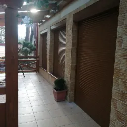 Zewnętrzne brązowe rolety zamontowane na elewacji budynku z cegieł, widok z zadaszonego tarasu z drewnianą konstrukcją.