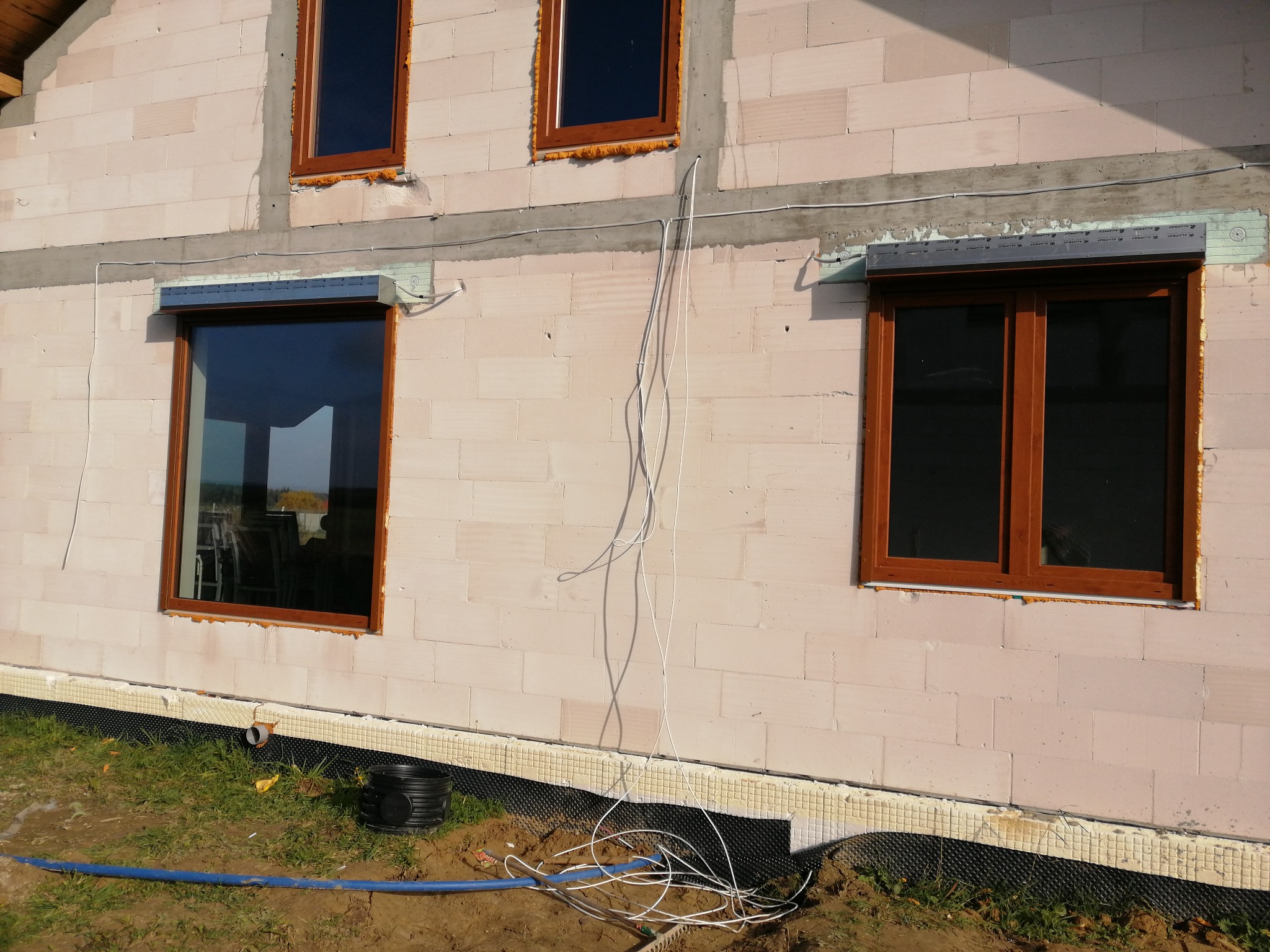 Montaż zewnętrznych osłon okiennych na surowej elewacji budynku z widocznymi kablami i elementami instalacji.