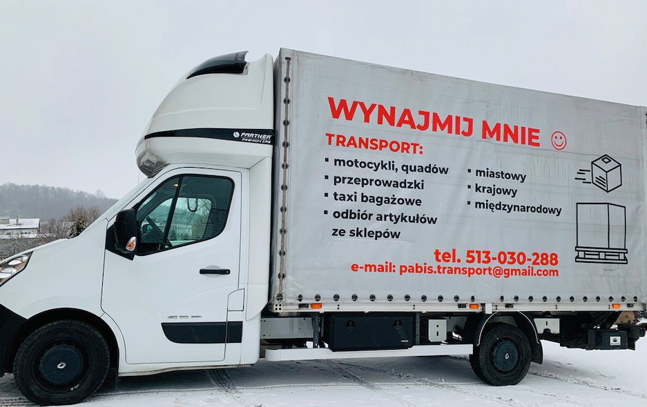 Biały samochód dostawczy z reklamą usług transportowych, w tym przeprowadzek, na boku naczepy, stojący na śniegu.