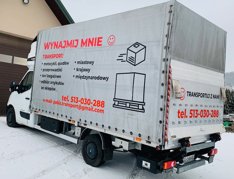 Biały samochód dostawczy z plandeką, na której widnieje napis 'Wynajmij mnie' oraz numer telefonu i adres e-mail firmy transportowej, zaparkowany na śniegu.