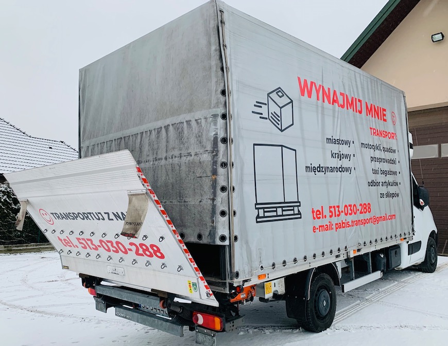 Ciężarówka z otwartą klapą załadunkową na śniegu, reklama firmy transportowej z numerem telefonu i adresem e-mail na plandece.