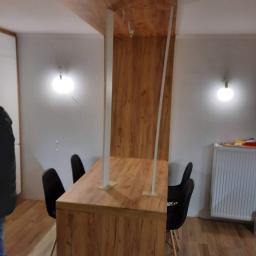 M&A DESIGN - Jadalnia z blatem i elementami ściennymi w odcieniach drewna, czarne krzesła, białe ściany i kaloryfer.