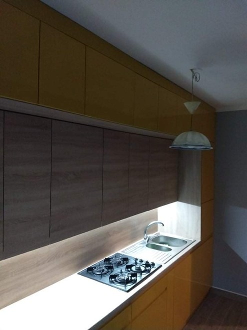 Żółto-brązowa kuchnia na wymiar z oświetleniem LED pod szafkami, widoczny zlew i płyta gazowa.