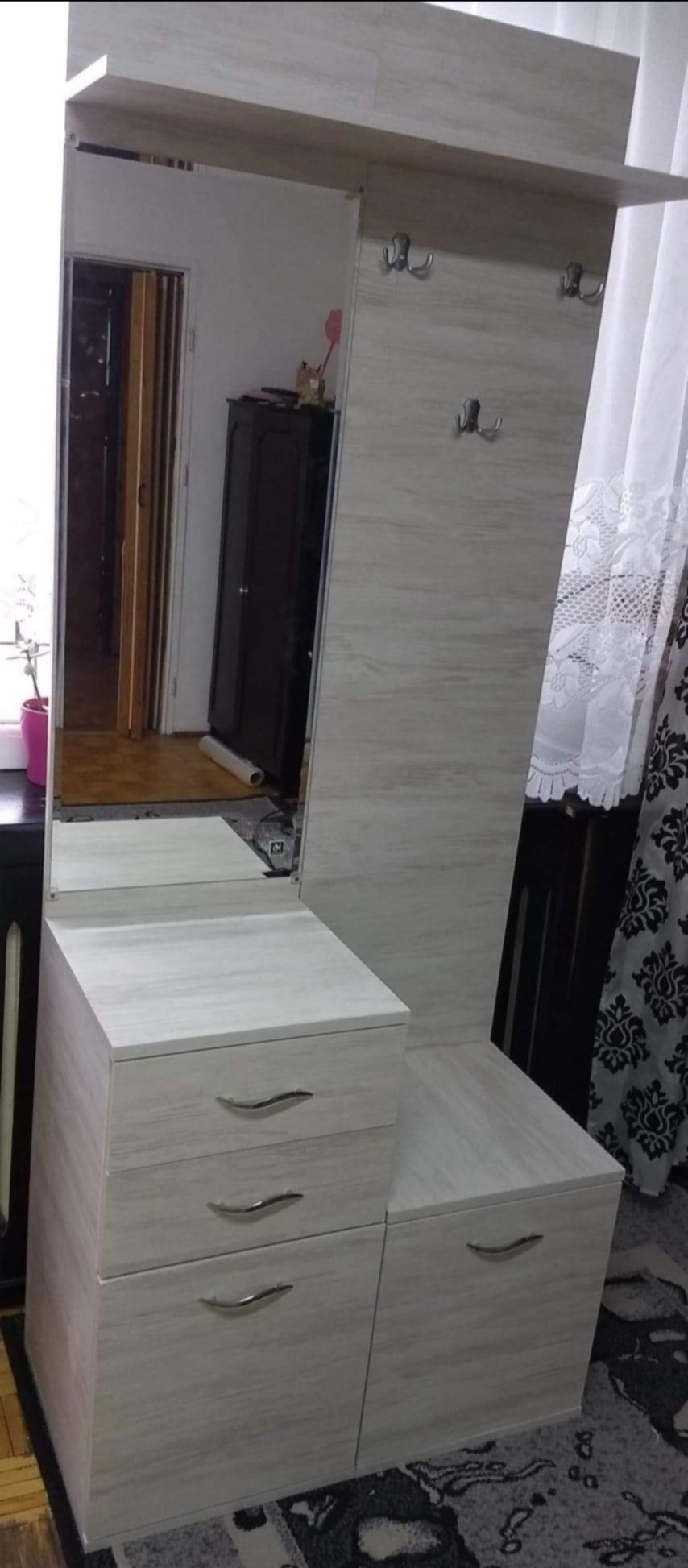 Jasna szafka z szufladami i lustrem z wieszakami w przedpokoju, widoczne odbicie wnętrza mieszkania.