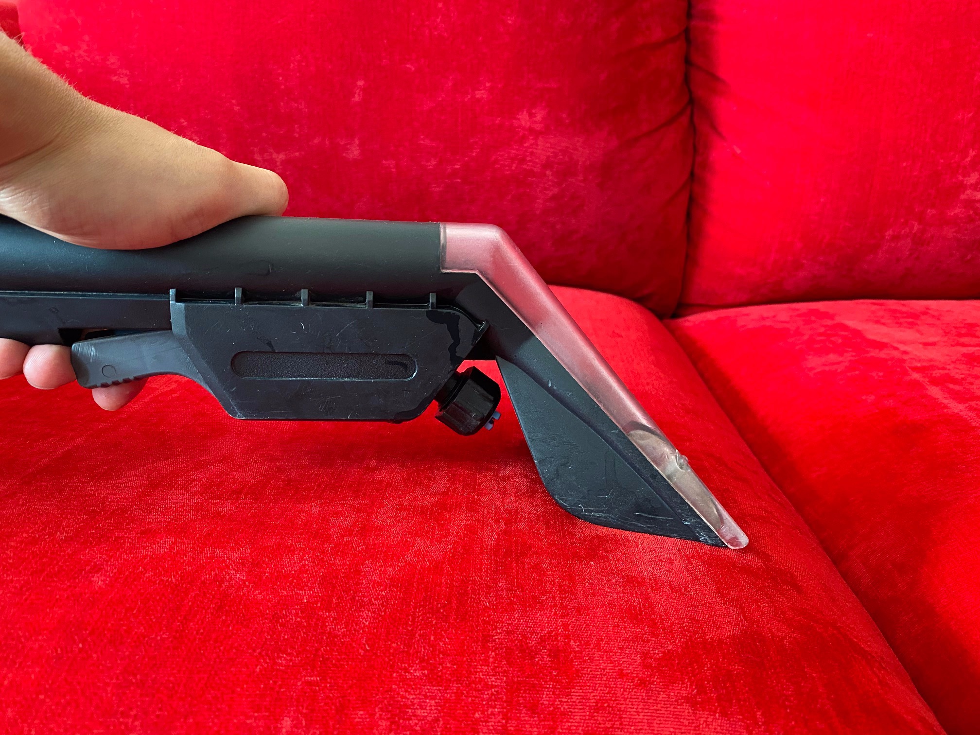 Czyszczenie czerwonej, welurowej sofy przy użyciu profesjonalnego odkurzacza piorącego z przezroczystą dyszą.