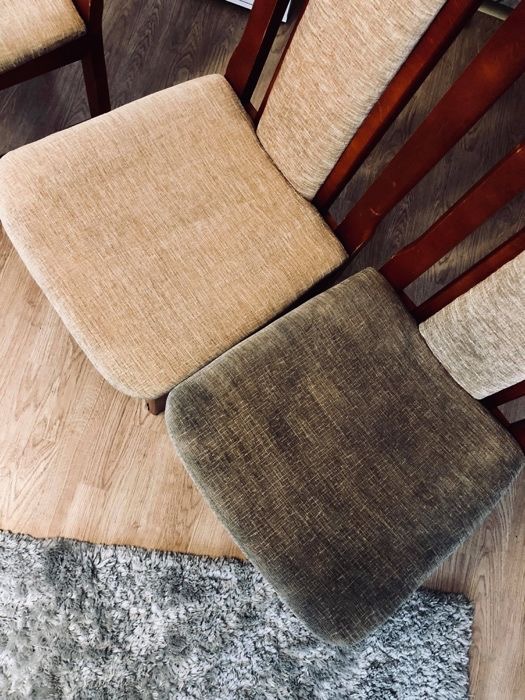 Dwa krzesła z tapicerowanymi siedziskami, jedno beżowe i czyste, drugie brązowe i wyraźnie zabrudzone, na drewnianej podłodze obok szarego dywanu.