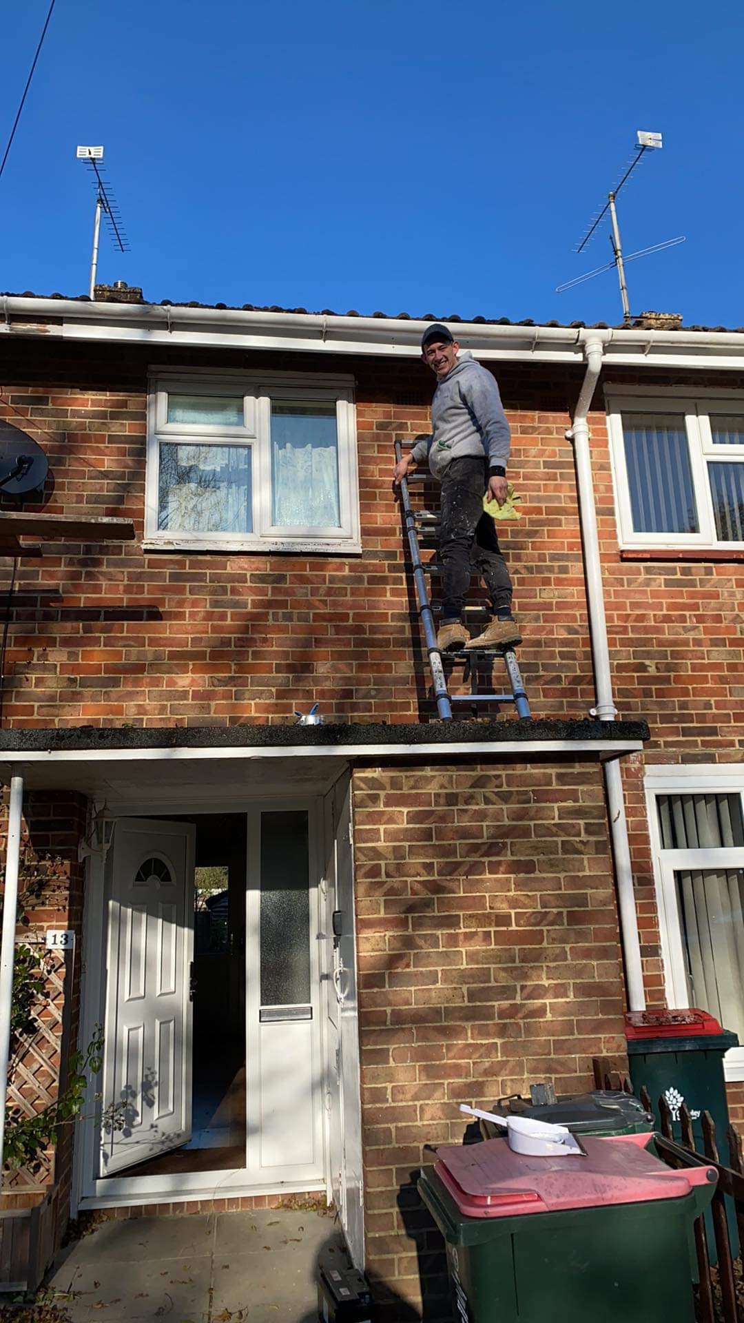 Mężczyzna na drabinie przy ceglanym domu, trzymający żółtą szmatkę, prawdopodobnie podczas prac związanych z elewacją.