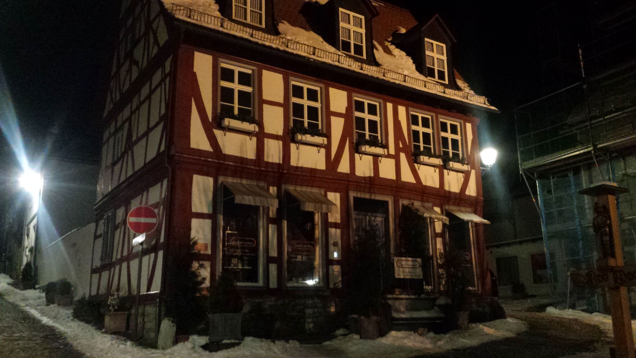 Nocny widok na trzykondygnacyjny budynek z muru pruskiego z czerwonymi belkami, śniegiem na dachu i zakazem wjazdu po lewej stronie.
