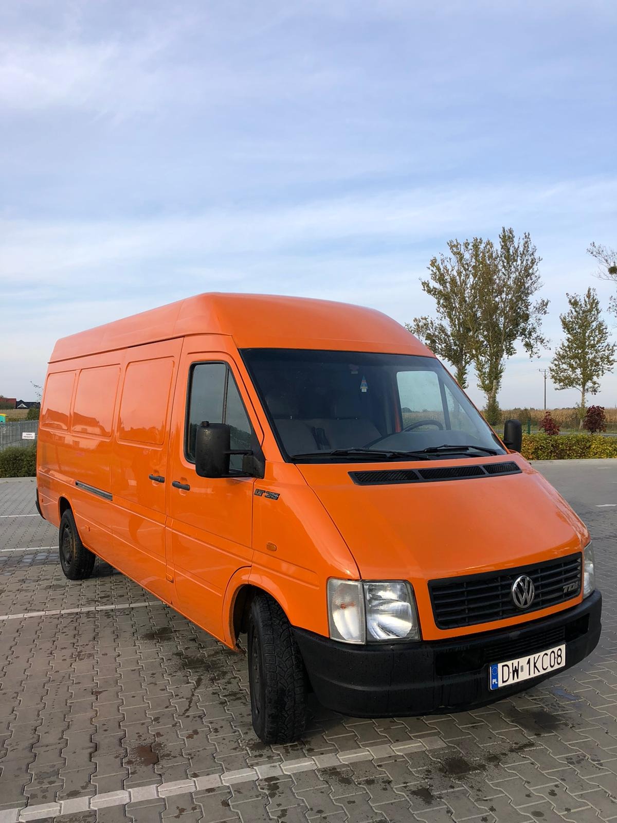 Pomarańczowy Volkswagen LT 35 na parkingu z kostki brukowej, błękitne niebo w tle.