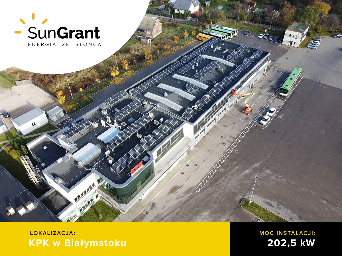 Widok z lotu ptaka na duży budynek z zainstalowaną instalacją fotowoltaiczną o mocy 202,5 kW. Moduły JA Solar 320 Wp black i inwertery Solis na dachu KPK w Białymstoku. Na parkingu autobusy...