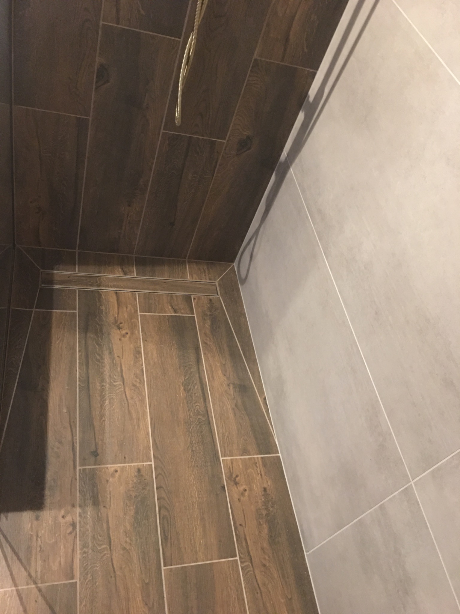 Wykończona kabina prysznicowa z odpływem liniowym, wyłożona płytkami imitującymi drewno na podłodze i szarymi płytkami na ścianach.