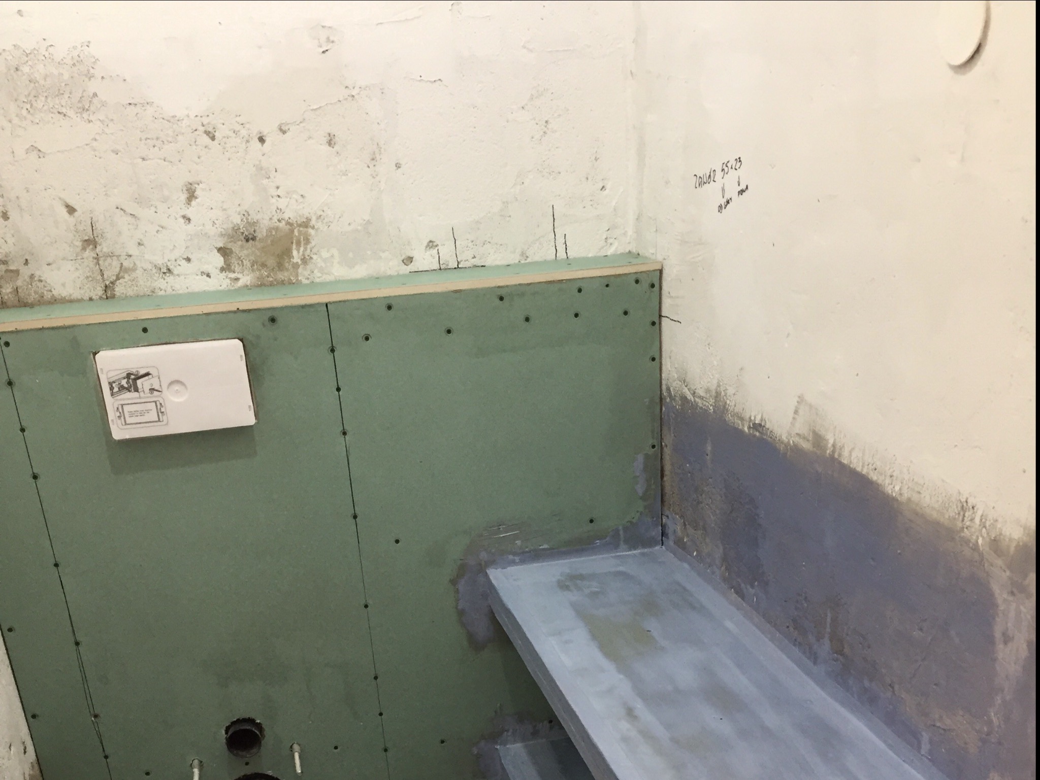Ściana łazienki w trakcie przygotowań do remontu: widoczne płyty kartonowo-gipsowe na konstrukcji, uszczelnienie hydroizolacyjne w rogu, oraz fragment instalacji podtynkowych.