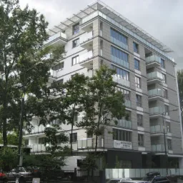 Nowoczesny budynek apartamentowy z balkonami i przeszklonymi balustradami, zlokalizowany w Warszawie na Powiślu przy ulicy Fabrycznej, widziany z poziomu ulicy w pochmurny dzień.