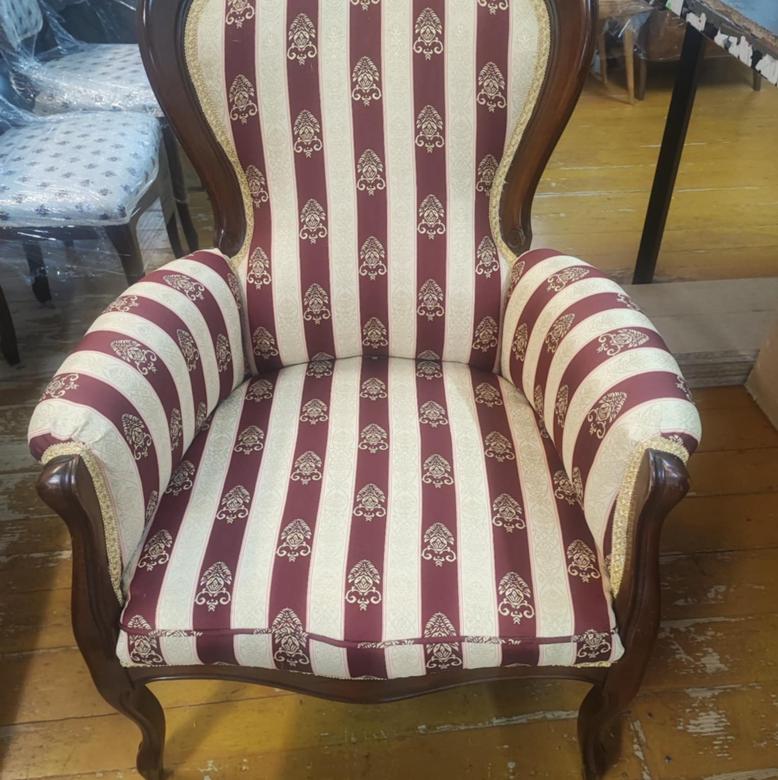 Odrestaurowany fotel w stylu vintage z bordowo-kremową tapicerką w paski i wzory, z ciemnobrązową ramą i złotymi zdobieniami, stojący na drewnianej podłodze.