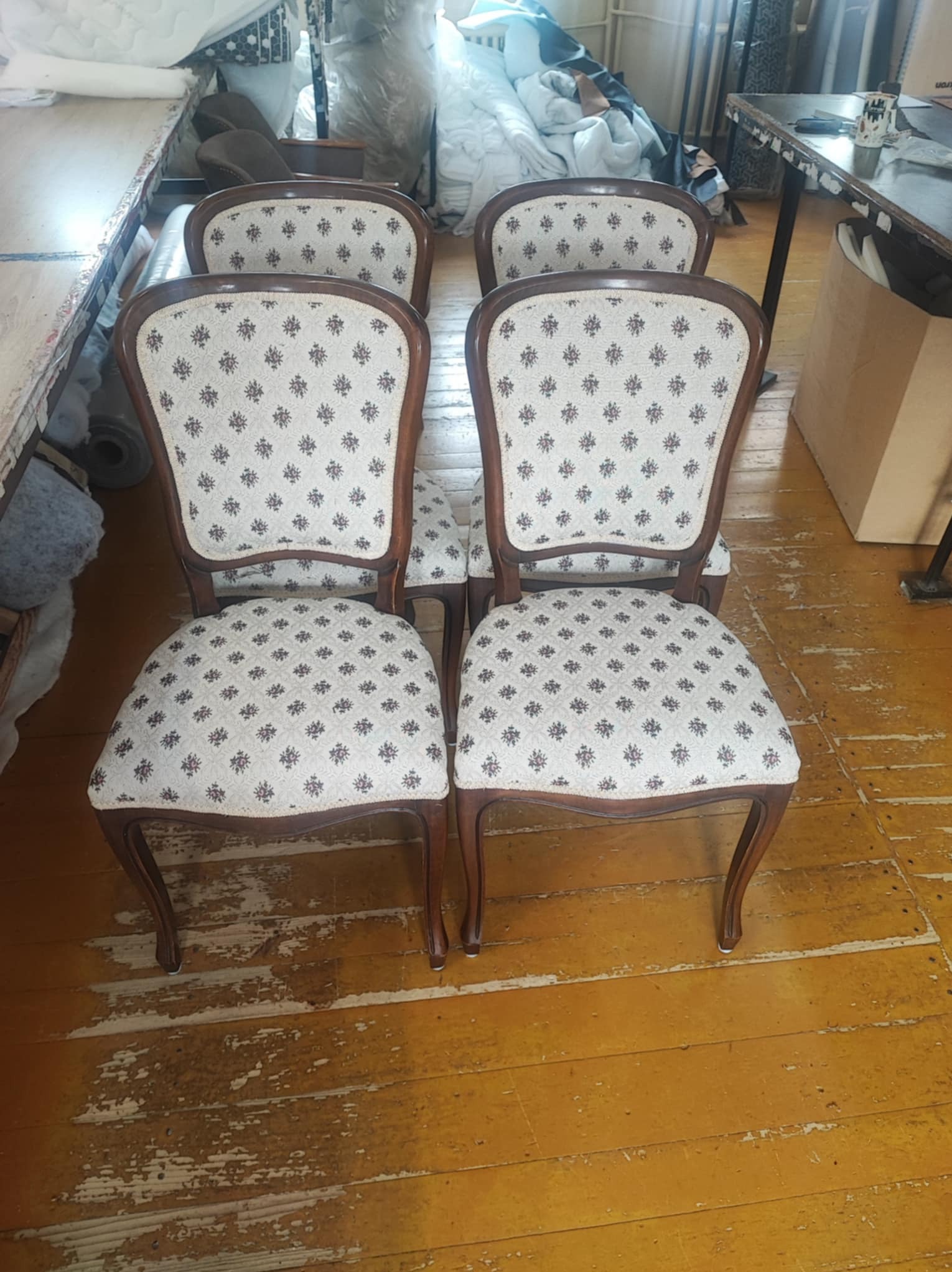 Cztery krzesła po renowacji tapicerskiej, z kremową tkaniną w drobne wzory, ustawione na podłodze z widocznymi śladami użytkowania. Widok z przodu, częściowo widoczne otoczenie warsztatu.