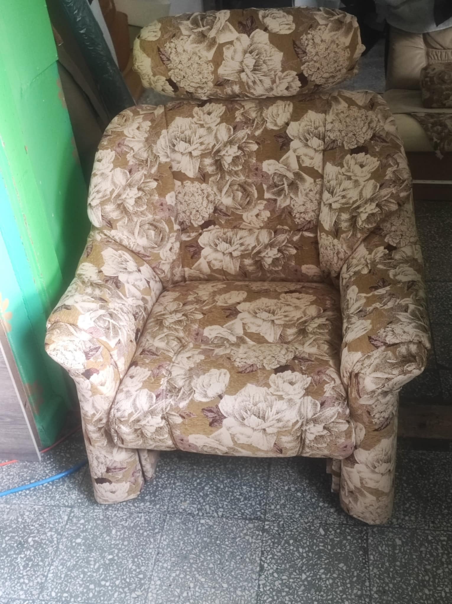 Kwiatowy fotel z wysokim oparciem i podgłówkiem, wzór w beżach i bieli, widok z przodu na szarym tle. Klasyczny mebel po renowacji.